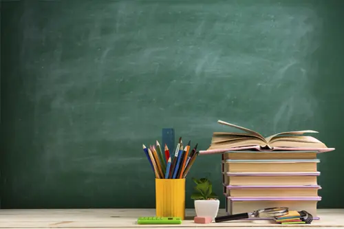 Przybory szkolne i otwarta książka na tle klasy – symbol warsztatów edukacyjnych dla dzieci i młodzieży.