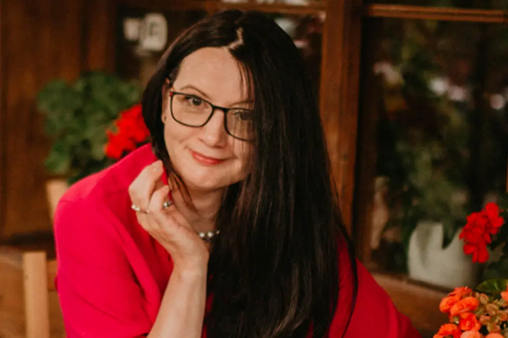 Trenerka rozwoju osobistego Iwona, współprowadząca warsztaty artystyczne, na portrecie w otoczeniu czerwonych kwiatów.