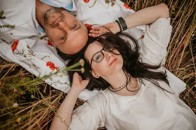 Iwona i Marek – prowadzący warsztaty rozwojowo-artystyczne, odpoczywających wspólnie na kocu wśród polnych kwiatów, symbolizujący autentyczność, bliskość i kontakt z naturą.