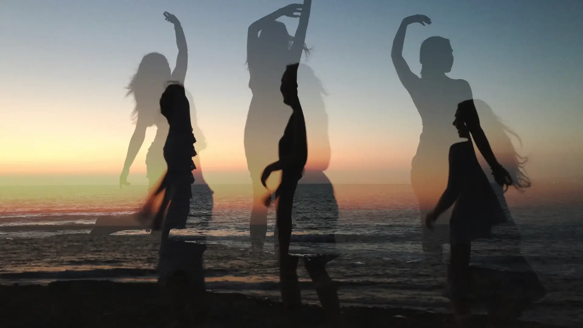 Osoby tańczące swobodnie nad brzegiem morza, oddające się ekspresji ruchu podczas tańca intuicyjnego.